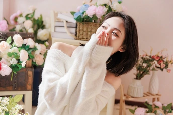 一个穿着白色长袍的年轻女子坐在桌子前的椅子上 桌子上摆满了花。