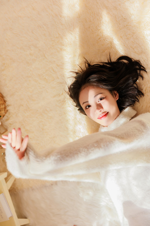 一个长着白头发站在床上的年轻女子 伸开双臂 床上有只泰迪熊。
