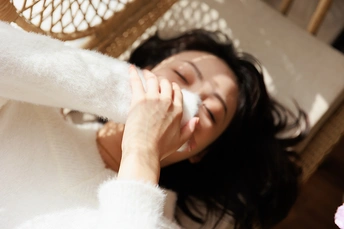 一位年轻女子躺在白色床上 用手捂住脸