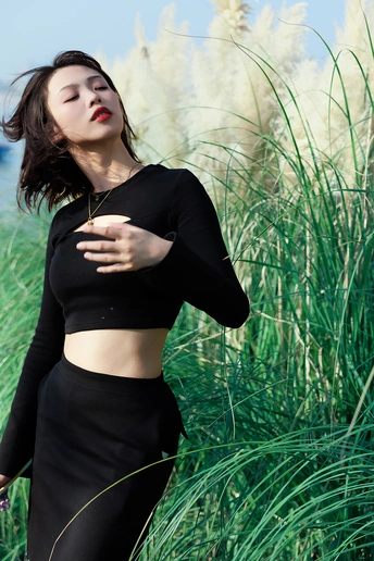 一个美丽的年轻女子穿着黑色上衣站在一片高草地上