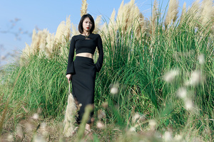 一个穿着长黑色连衣裙的女孩站在一片高草丛中