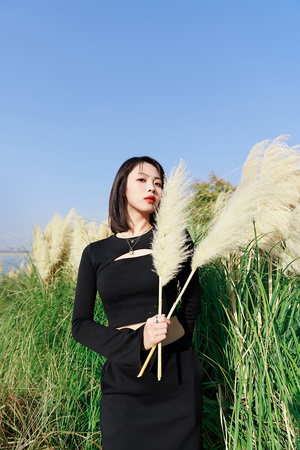 一个穿着黑色连衣裙的年轻女子站在一片高草丛中 伸出手向旁边。