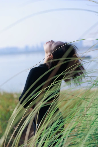 站在水边附近的一片 tall grass 中的年轻女子