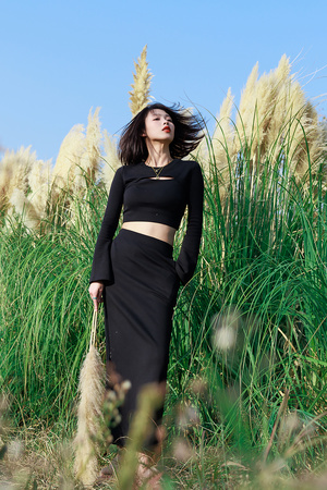 一位美丽的年轻女子穿着黑色上衣和裙子站在一片高草地上