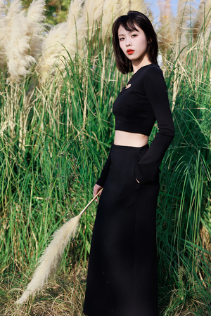 一位穿着黑色长裙的年轻女子站在高草前面