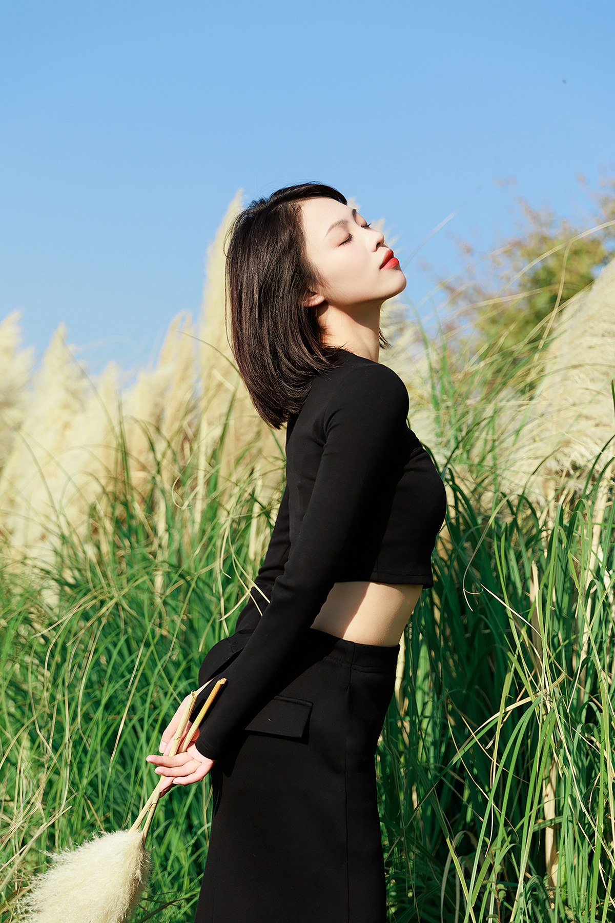 一位穿着黑色连衣裙的女子站在一片高草丛中