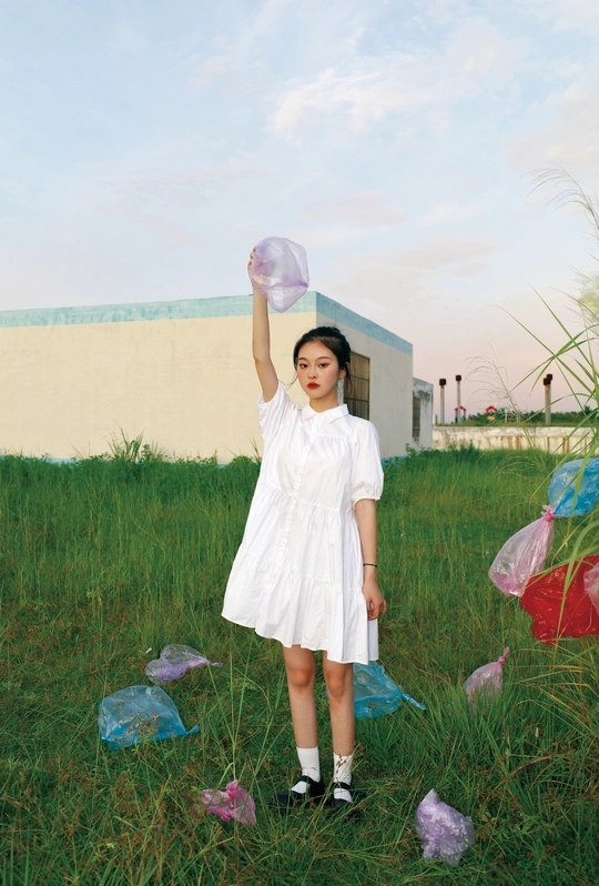 一个穿着白色连衣裙、拿着塑料袋的年轻女孩站在草地上