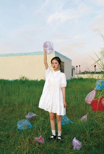 一个穿着白色连衣裙、拿着塑料袋的年轻女孩站在草地上