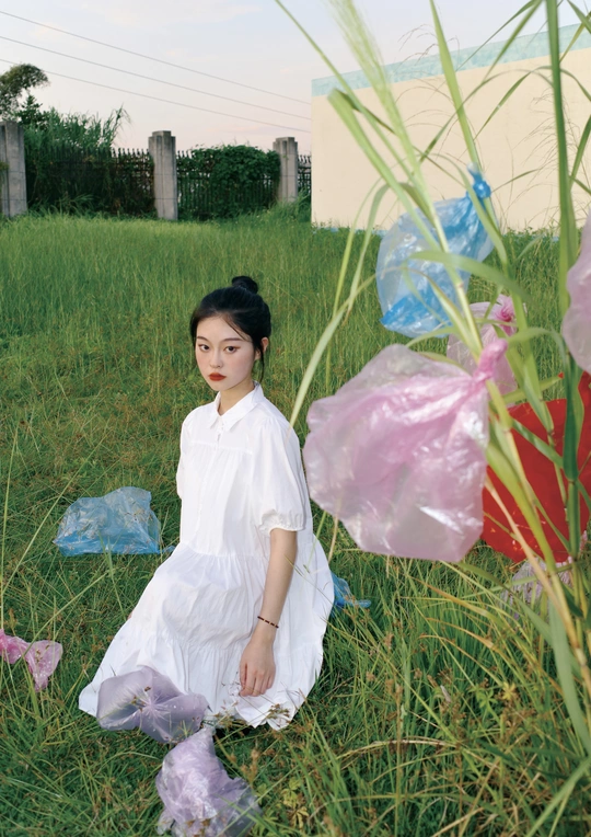 一位身穿白色连衣裙的年轻女子站在一片高高的草地上