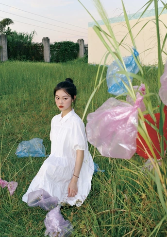 一位身穿白色连衣裙的年轻女子站在一片高高的草地上