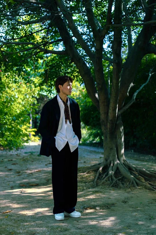 一个穿着袍子和领带站在树木丛生的小径上的年轻人
