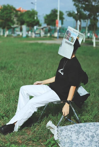 一个坐在草地上 戴着帽子 正在公园里阅读报纸的女人。