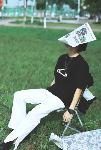 一位戴帽子正在公园草地上阅读报纸坐在椅子上的女士