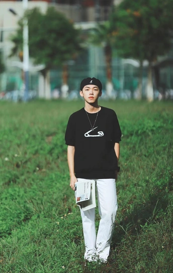 一个穿着黑色衬衫的年轻人站在一片绿色的草地上