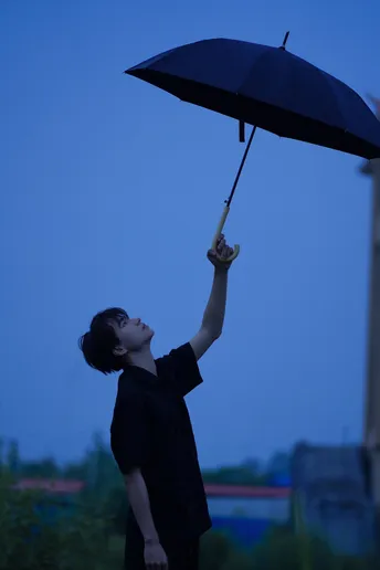 一位年轻人举着一把黑色雨伞向天空。