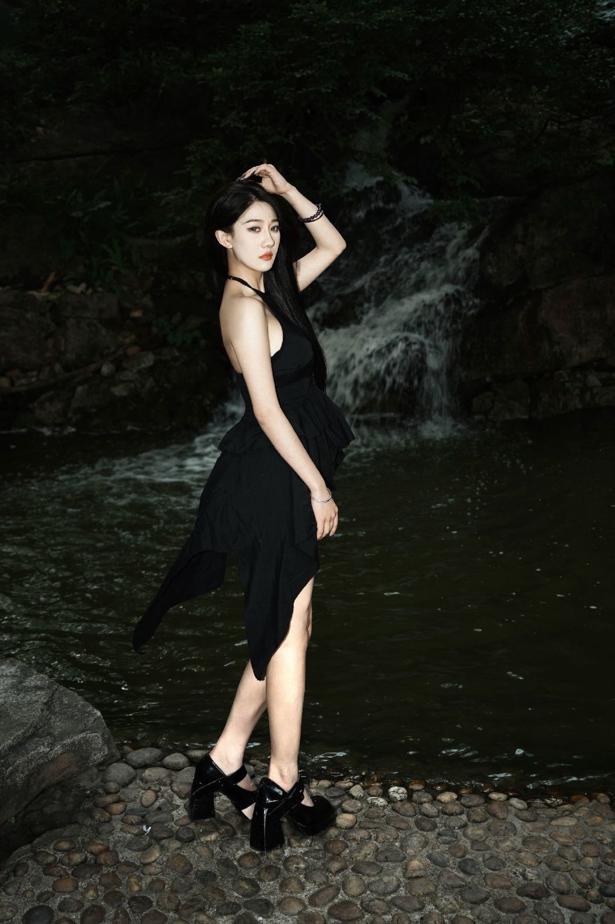 一个穿着黑色连衣裙的女人站在河中的岩石上