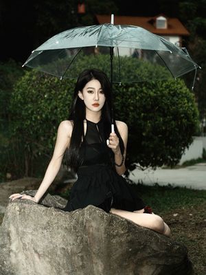 一个穿黑色连衣裙的女人拿着雨伞坐在岩石上