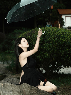 一个穿着黑色连衣裙的年轻女子 手里拿着一把伞 坐在岩石上。