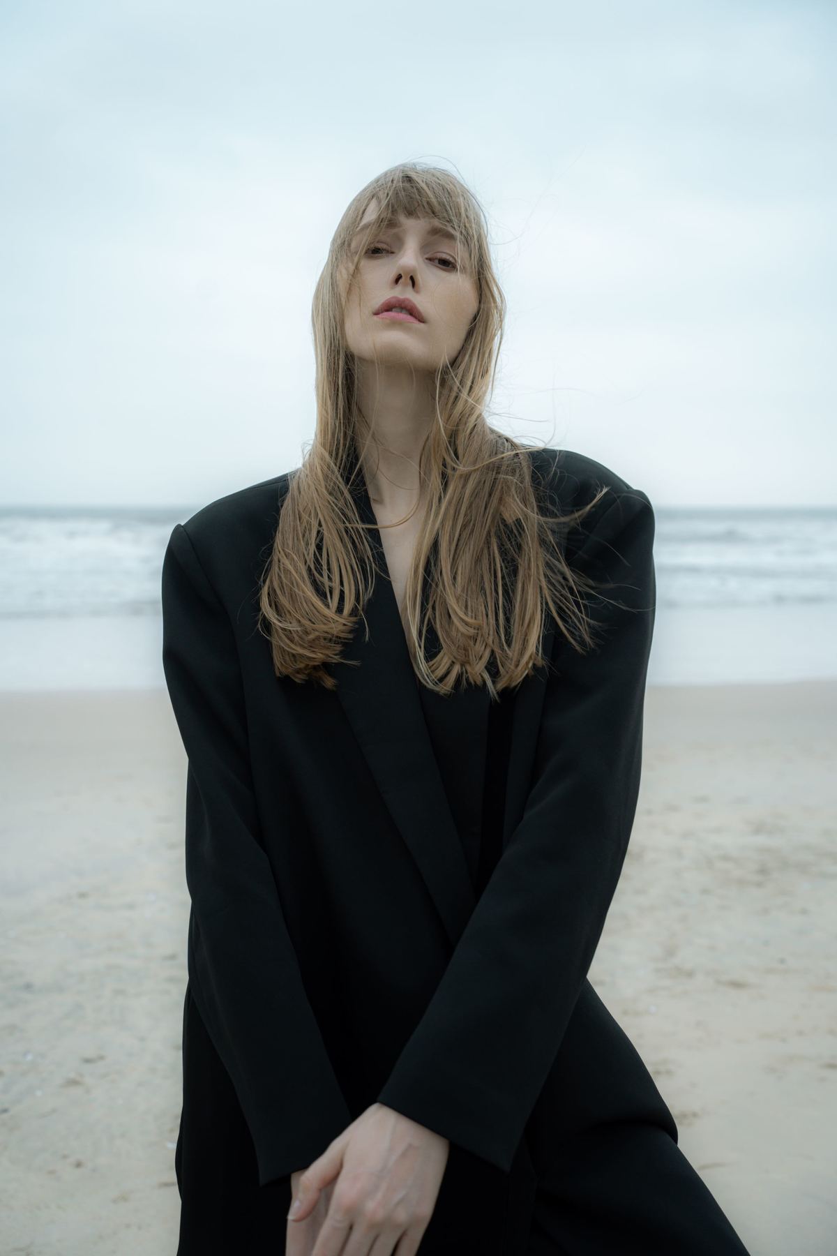 一位穿着黑色长外套的年轻女子在海滩上摆姿势