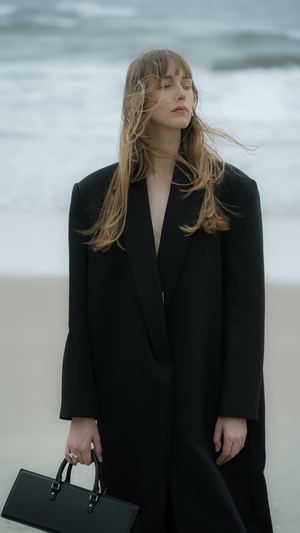 一位穿着黑色外套和包站在海滩上的模特