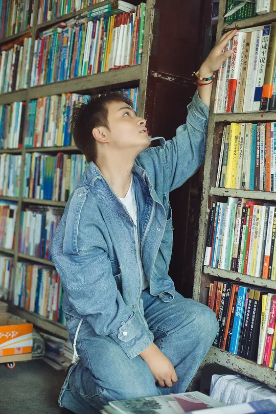 一个年轻人坐在书架前的一堆书上。