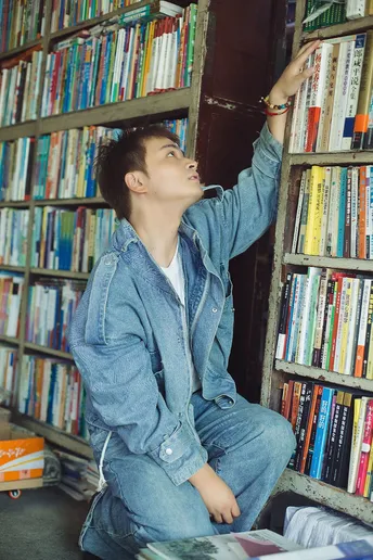 一个年轻人坐在书架前的一堆书上。