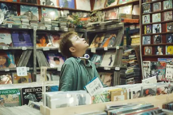 一个年轻的男孩站在一张桌子旁 书店里看着书。