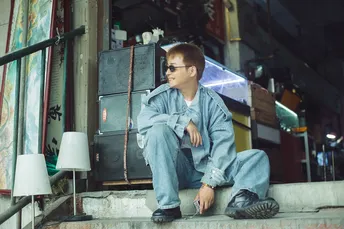 一个戴眼镜的年轻人坐在一些台阶上 前面是一座建筑。