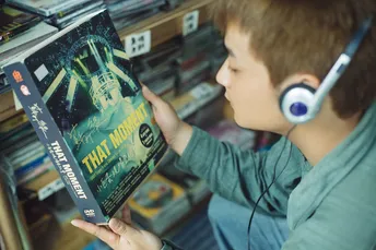 一个戴耳机的小男孩在DVD商店里看着DVD。