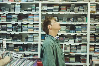 一个年轻男子站在一个书店里 面前是书架和CD架。