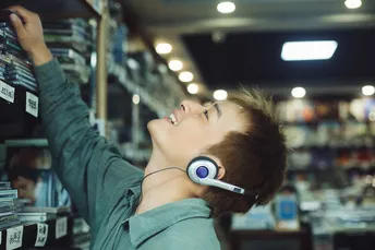 一个戴着耳机 young man 正在商店里看着书架上的书。