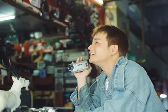 一个年轻男子坐在商店里的桌子旁 手里拿着一杯东西 正在给一只山羊拍照。