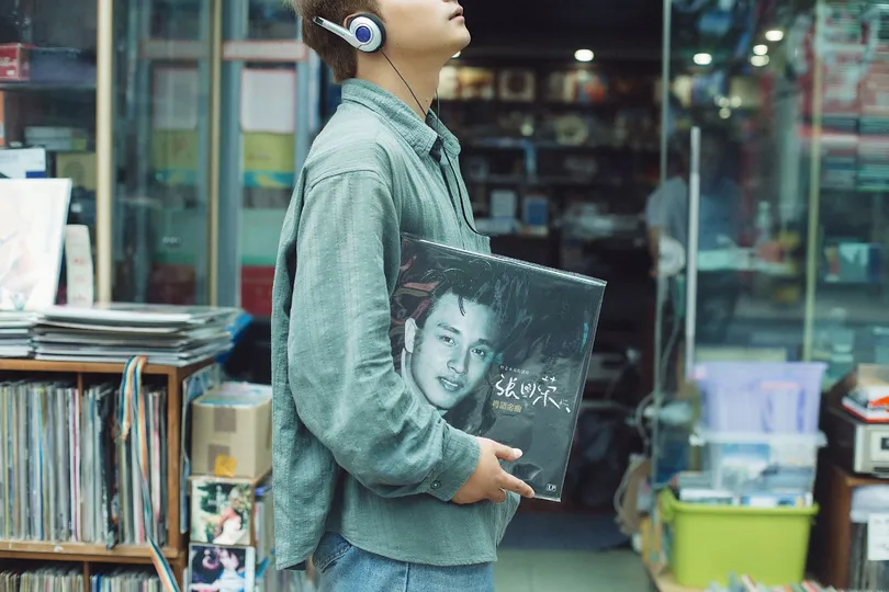 一个戴耳机 young man 穿行于书店 书店里摆满了书籍和 CD。