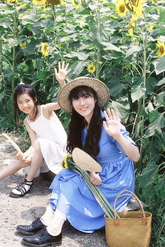 一位年轻女子和一个小女孩在花园里的向日葵田前摆姿势