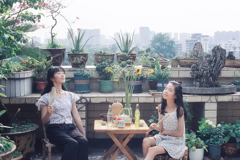 两位年轻女性坐在一个阳台上 前面有一个有盆栽的花园。