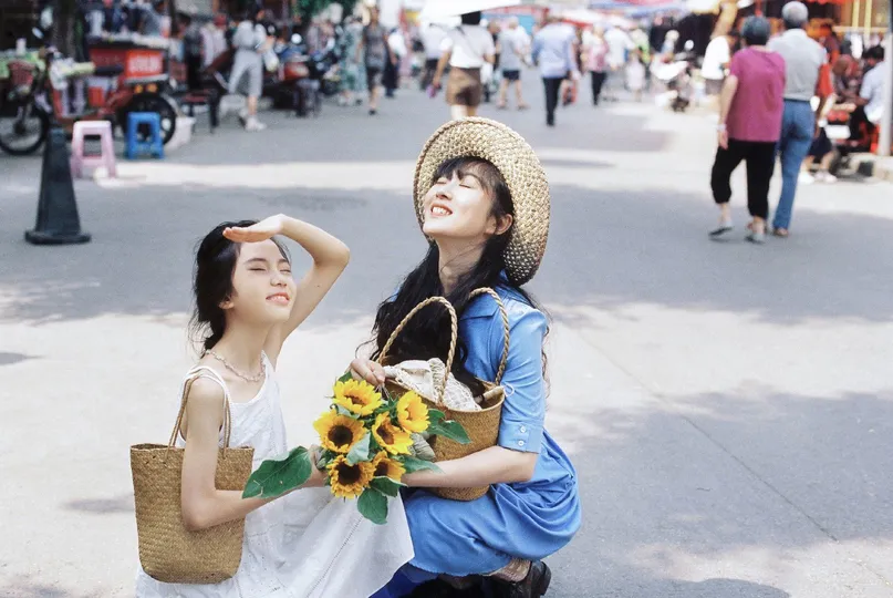 一位年轻女子抱着一个花篮 里面装满了向日葵 而一位年轻男子站在繁忙街道的人行道上。
