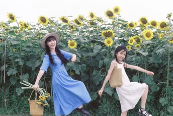 两个穿蓝色连衣裙的年轻女子走在向日葵花田中