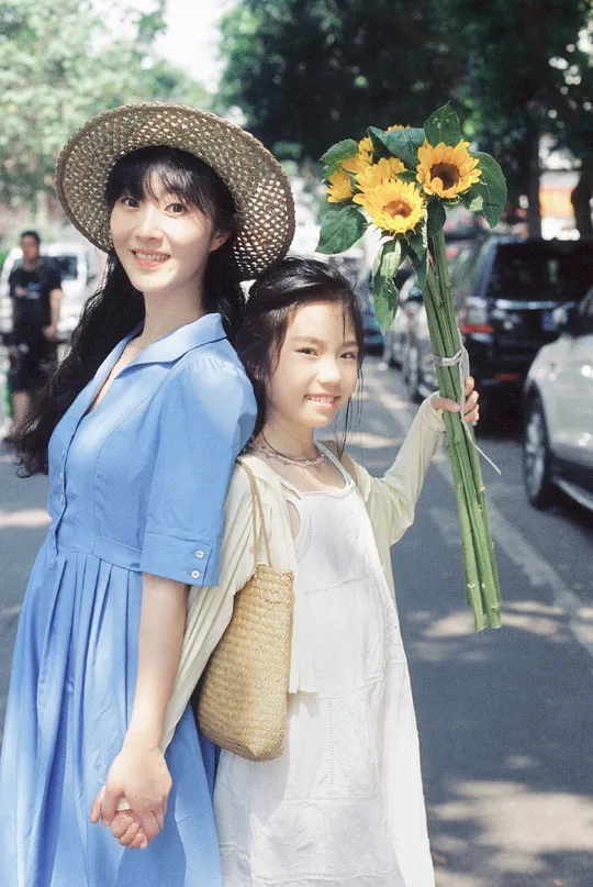 一位年轻女子和一个小女孩穿着蓝色衣服 手里拿着向日葵走在街上。