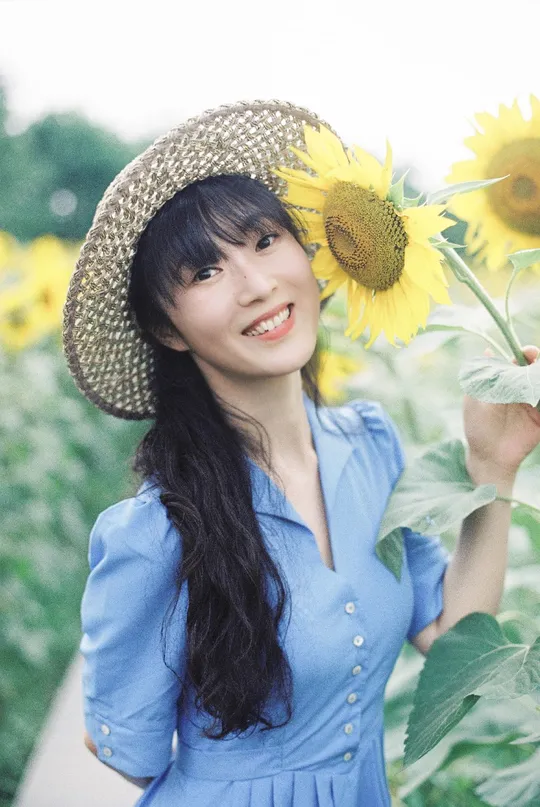 一位穿着蓝色连衣裙和草编帽子的年轻女子 在向日葵田里拿着向日葵。