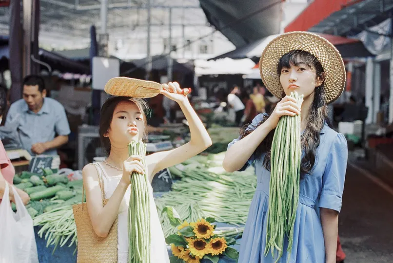 一位戴帽子的女士在市场上拿着一些蔬菜