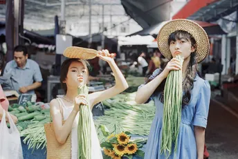 一位戴帽子的女士在市场上拿着一些蔬菜