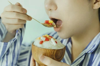 一个年轻男孩在一个木碗中吃米饭。