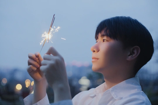 一个小男孩拿着点燃的烟花棒仰望天空 背景是一座城市。