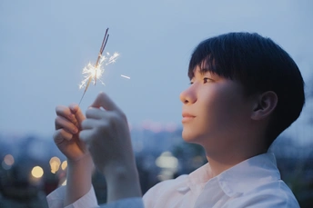 一个小男孩拿着点燃的烟花棒仰望天空 背景是一座城市。