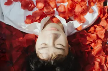 一个年轻女子将脸庞浸入盛满红色花朵的碗中 鲜花漂浮在她的头顶之上。