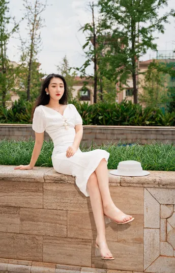 一个美丽的年轻女子穿着白色连衣裙坐在石头墙上