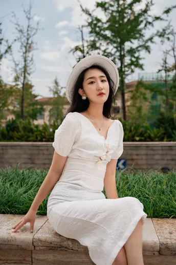 一位穿着白色连衣裙和帽子坐在长凳上的年轻女子