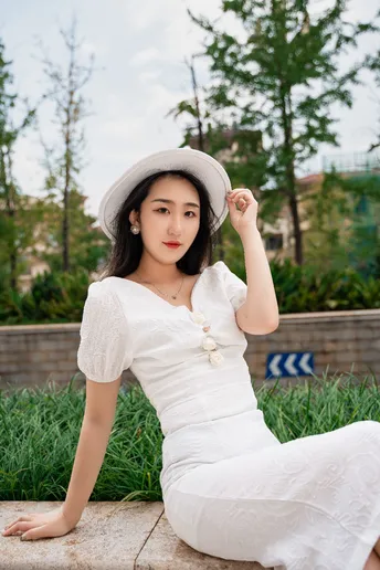一位美丽的年轻女子穿着白色连衣裙和帽子坐在墙上
