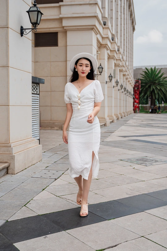 一位穿着白色连衣裙和帽子走在街道上的年轻女子