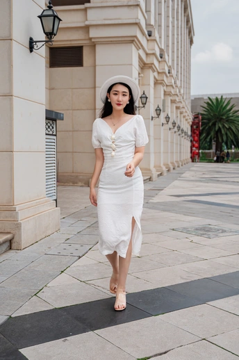 一位穿着白色连衣裙和帽子走在街道上的年轻女子